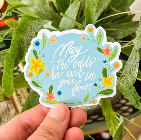 May the odds be ever in your favor sticker with flower drawing on plant